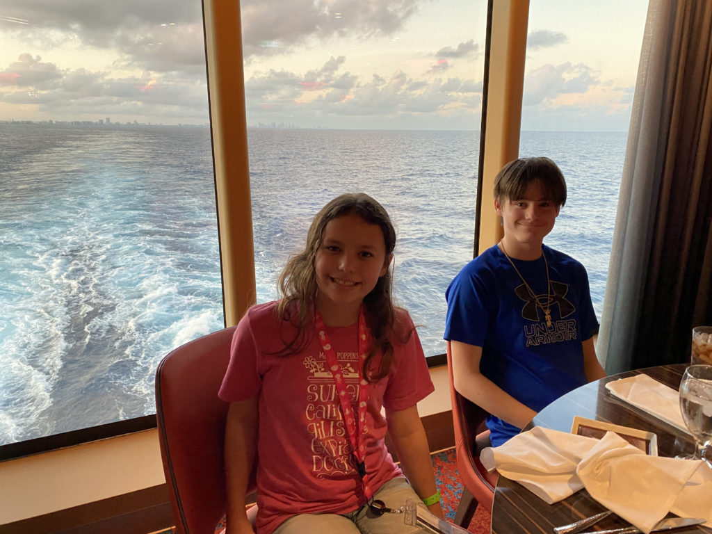 a couple of kids sitting at a table with a view of the ocean