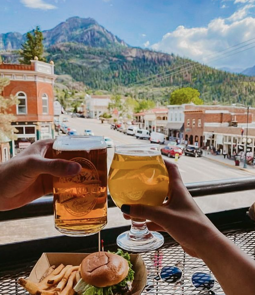 a couple of hands holding glasses of beer and a burger