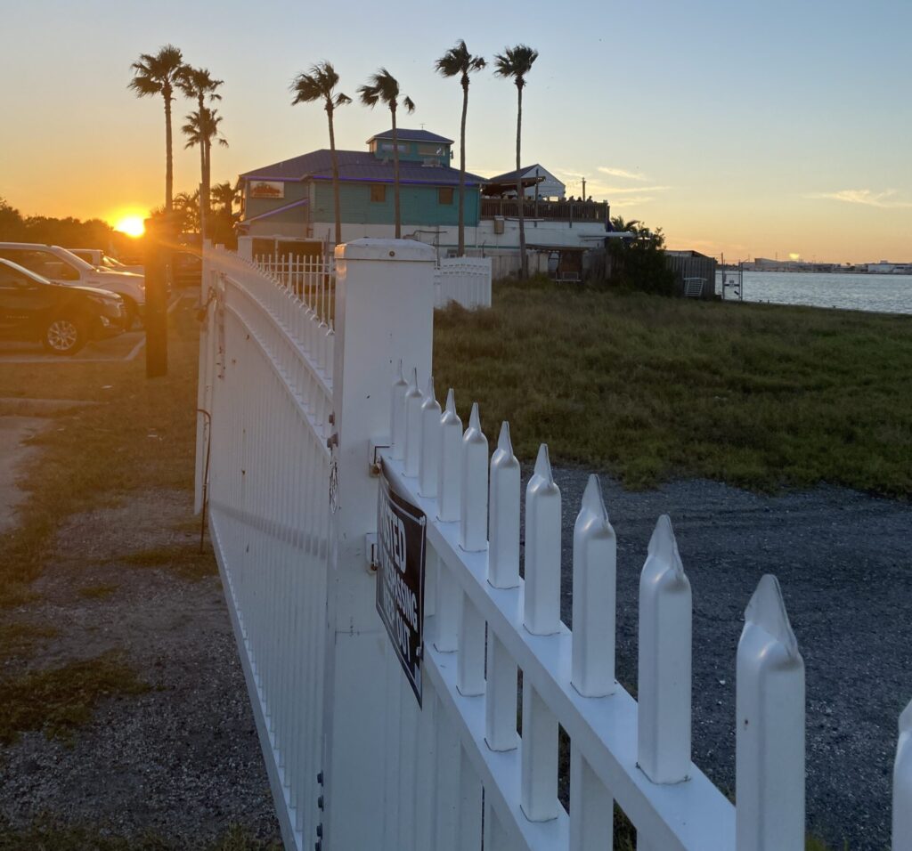 a white fence with palm trees and a building in the background