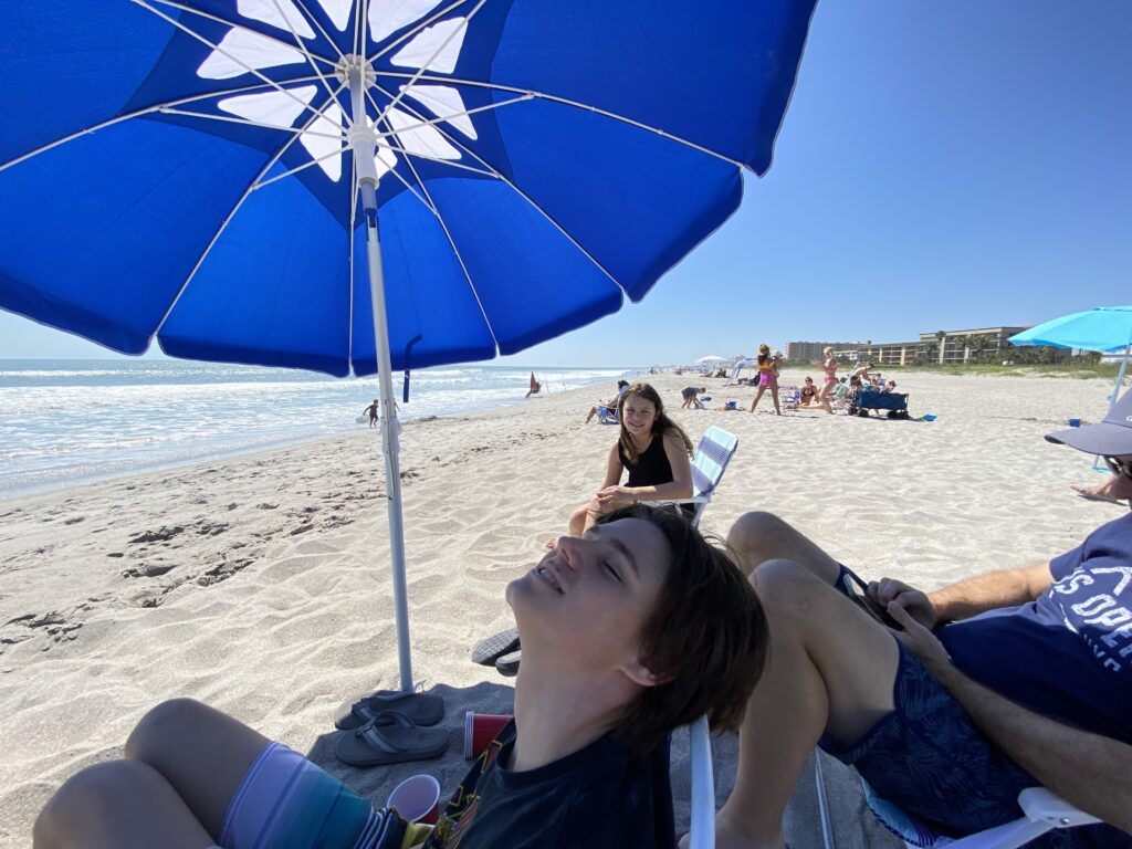 a group of people sitting under a blue umbrella on a beach