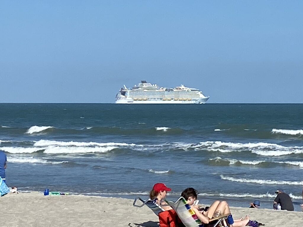 people sitting on a beach with a cruise ship in the background