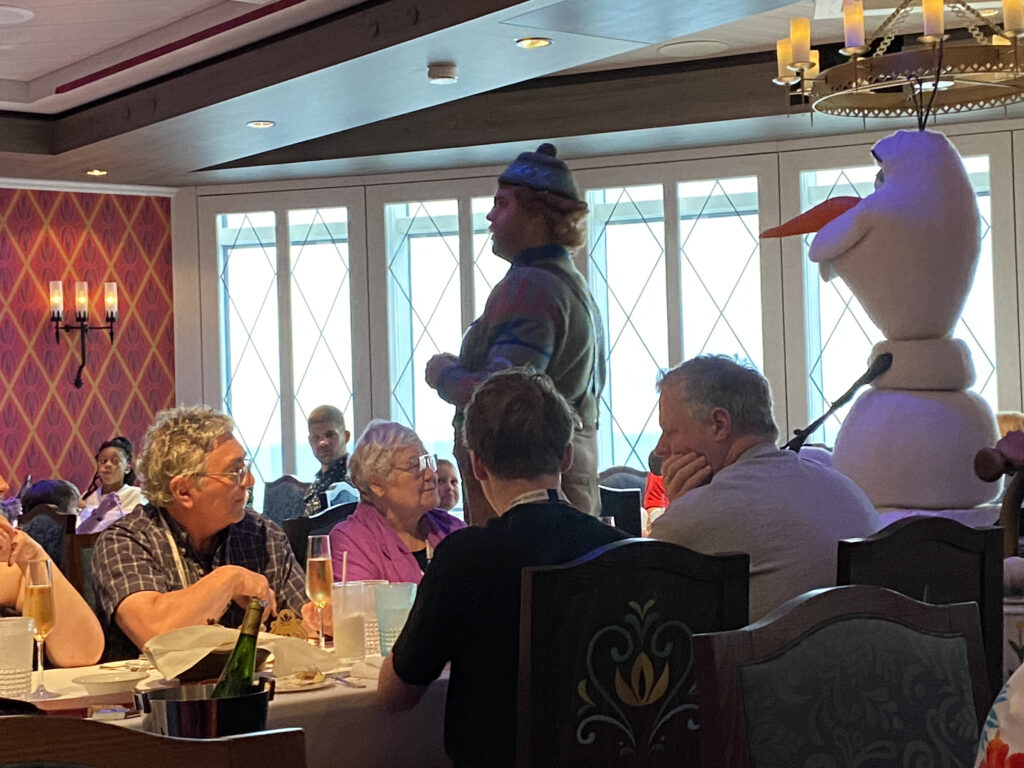 a person in garment standing in a room with people sitting around