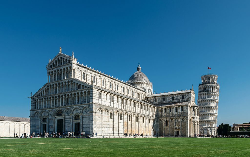 a large building with a large dome and a green lawn with Piazza dei Miracoli in the background