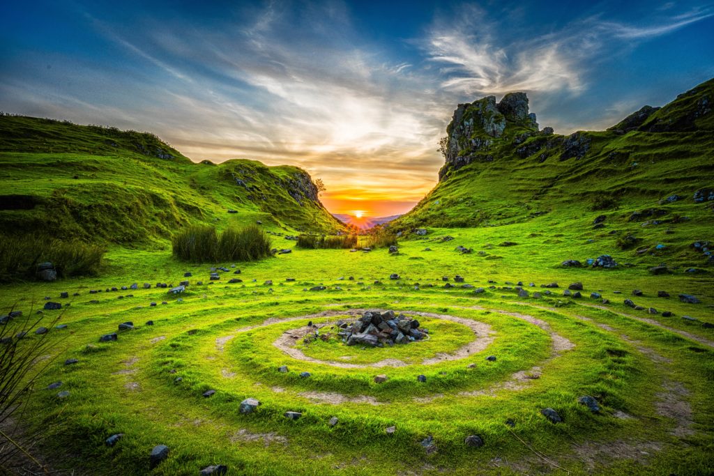 a circular green field with rocks and a fire pit