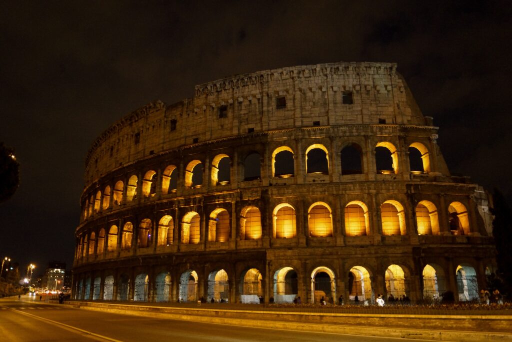 a large stone building with many arches with Colosseum in the background