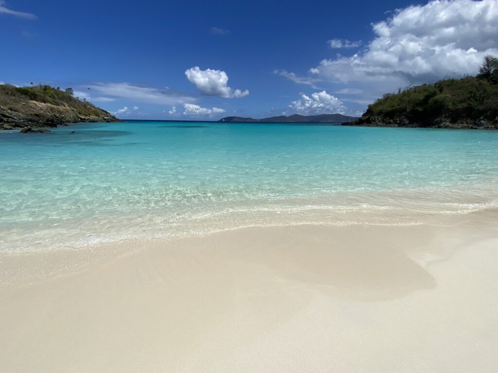 a beach with clear blue water and land and blue sky