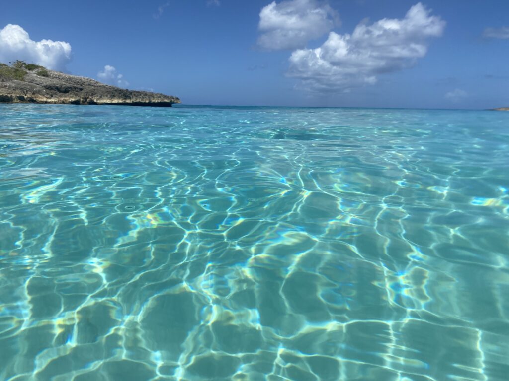 a clear blue water with a rocky island in the background