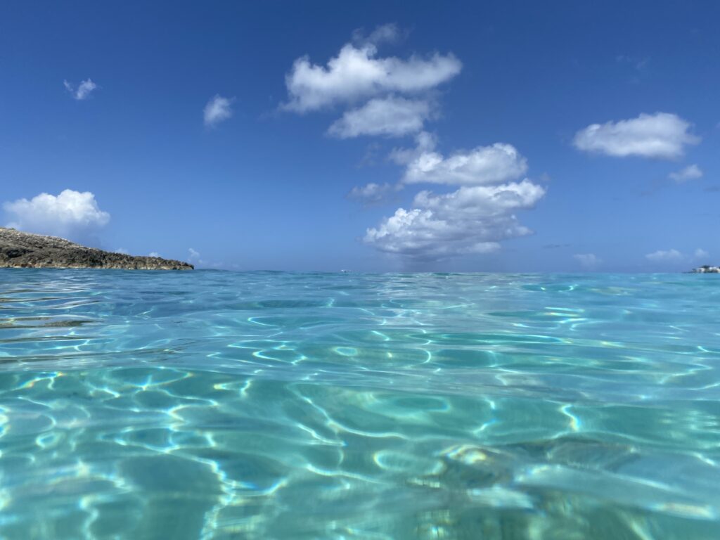 a clear blue water with a rocky island in the background