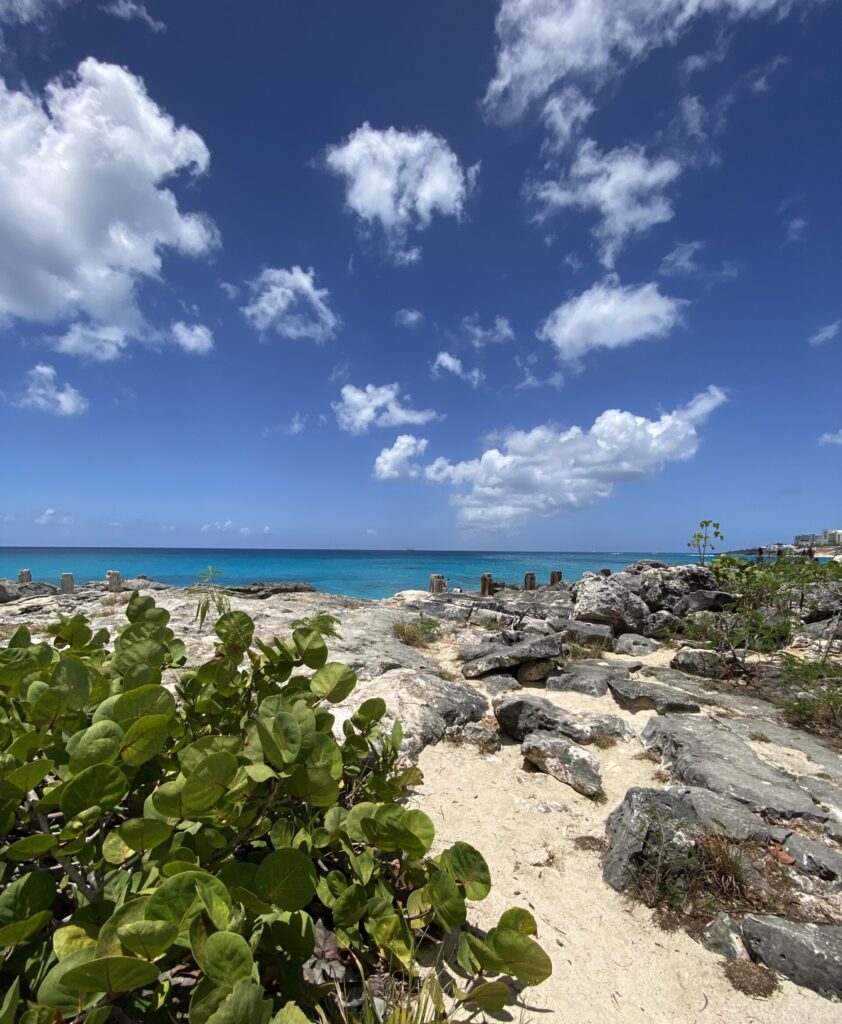 a rocky beach with blue water and clouds in the sky