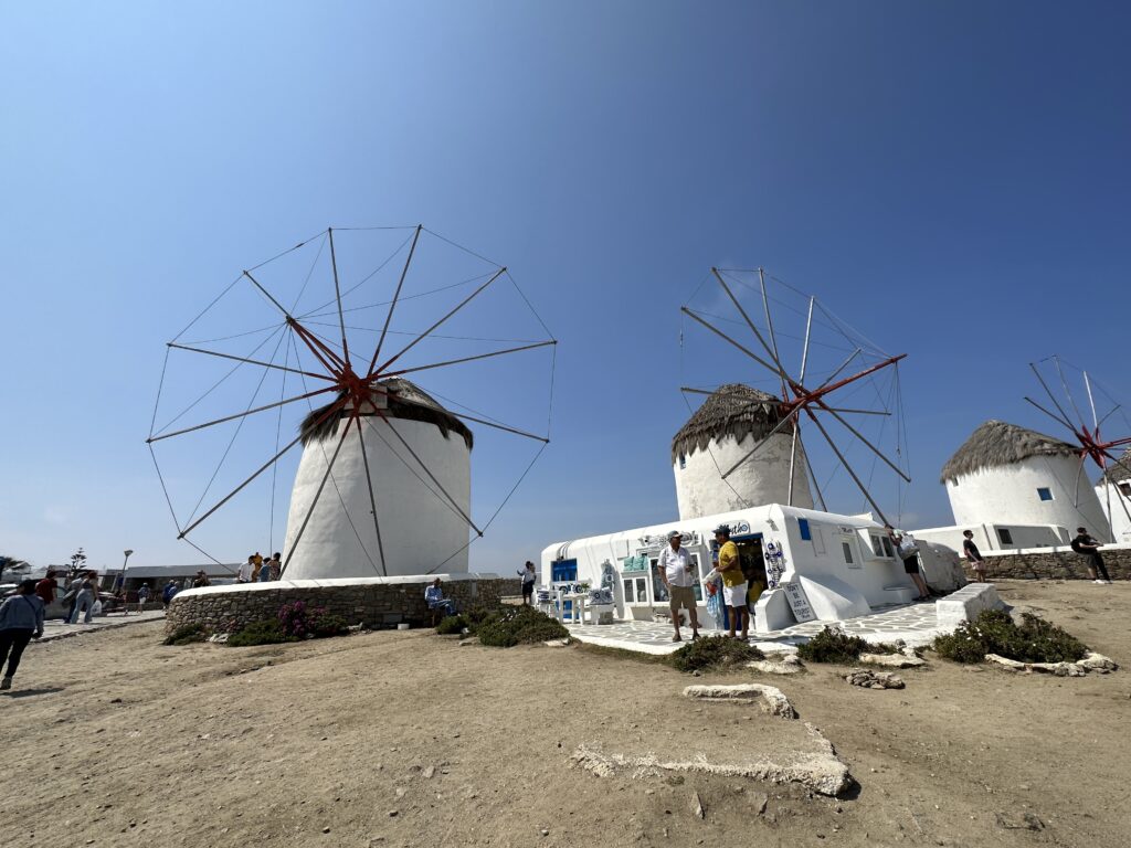 a group of windmills in a sandy area with Mykonos in the background