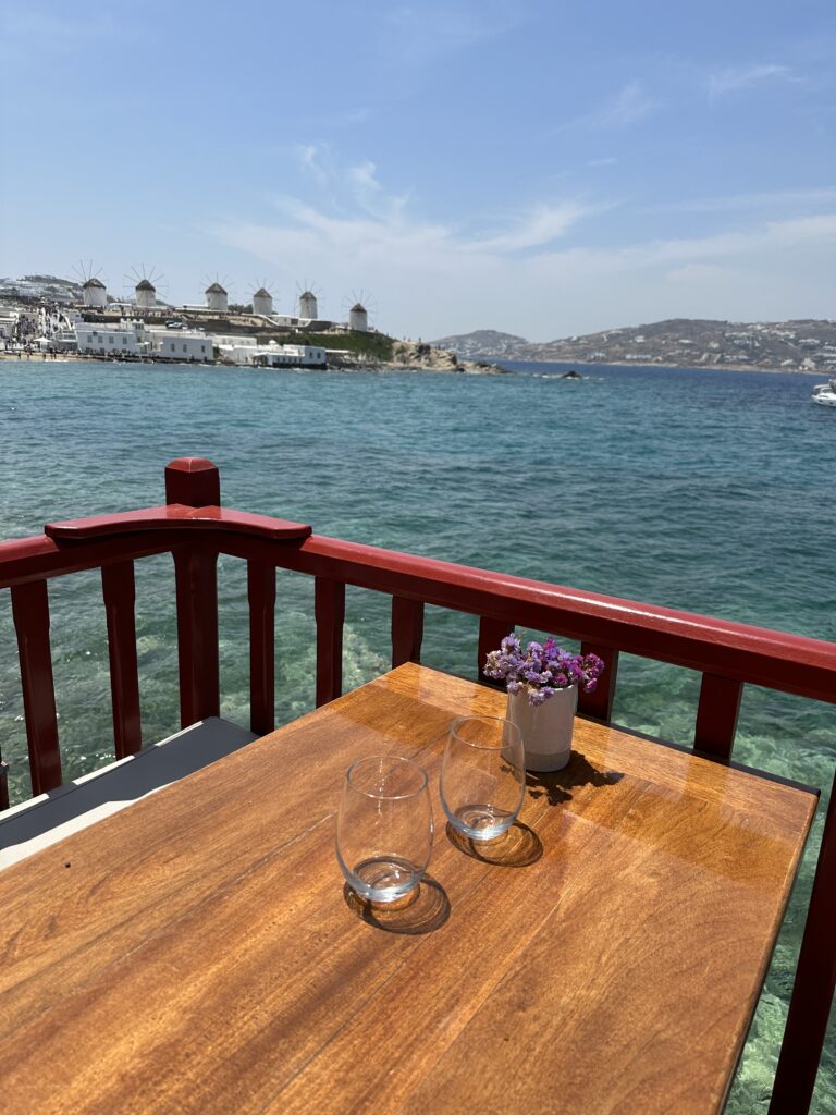 a table with wine glasses and flowers on a balcony overlooking water