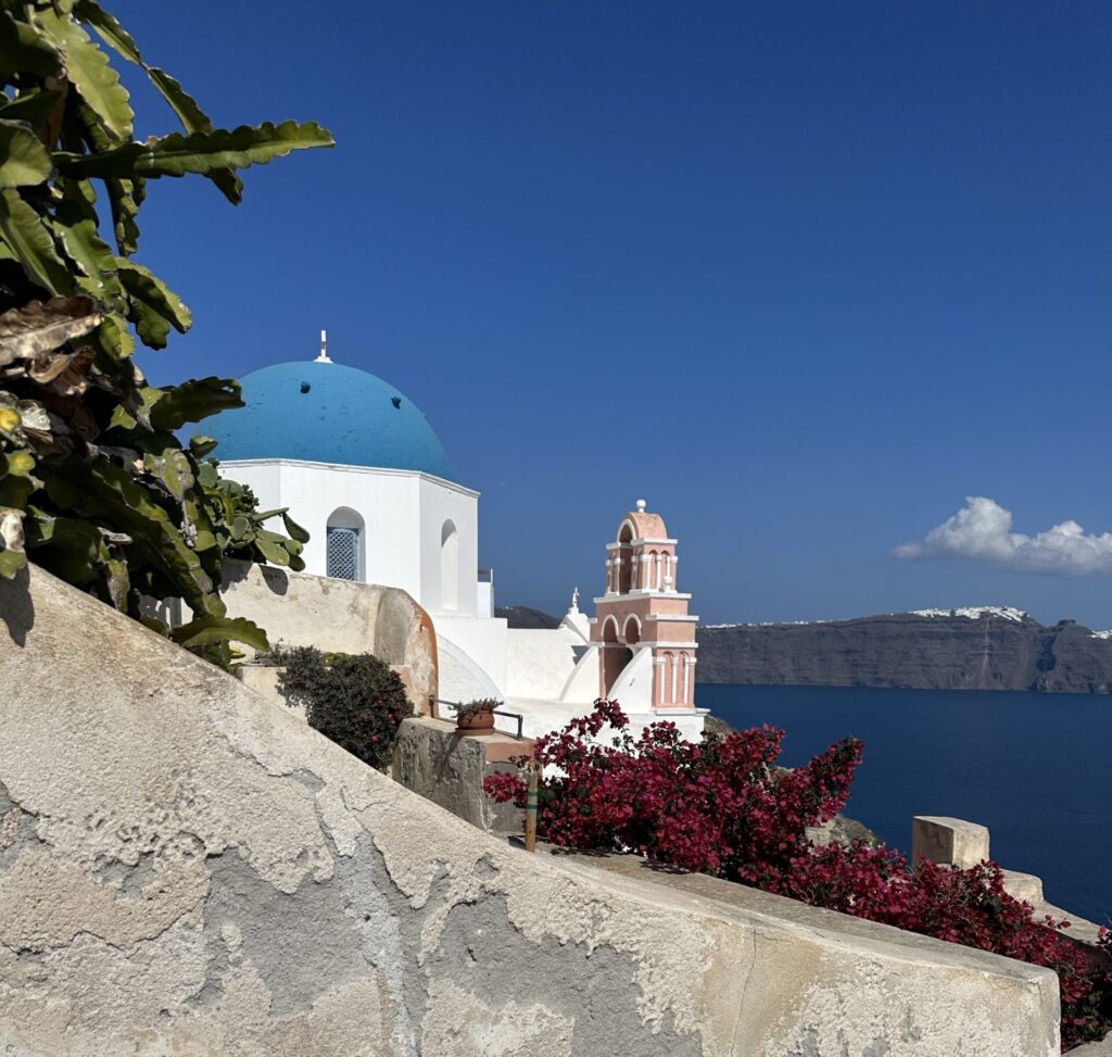 a white building with a blue roof and a blue dome on a cliff