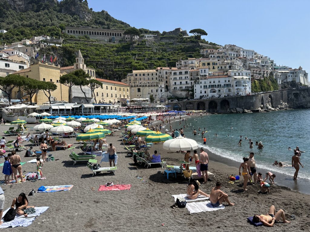 a beach with people and umbrellas and buildings on the side
