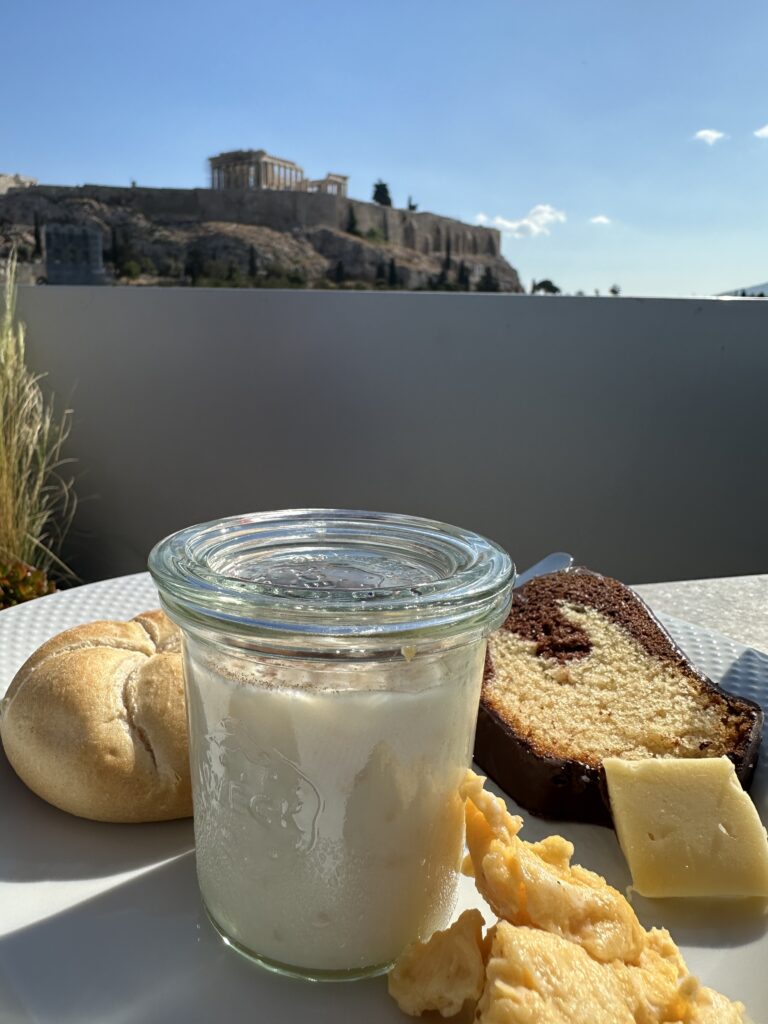 a glass jar of milk and bread on a table with a building in the background