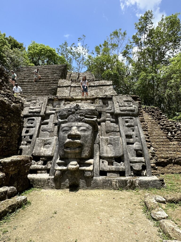 a stone structure with a face carved into it with Lamanai in the background