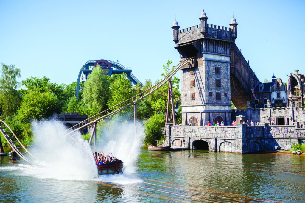 a boat on water with a tower and a roller coaster