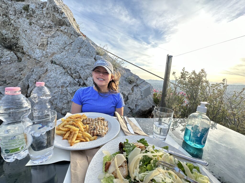 a woman sitting at a table with plates of food and water