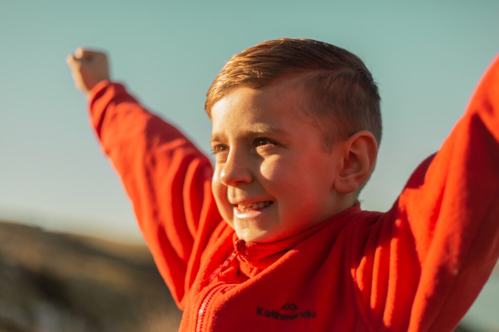 a boy in a red jacket with his arms raised