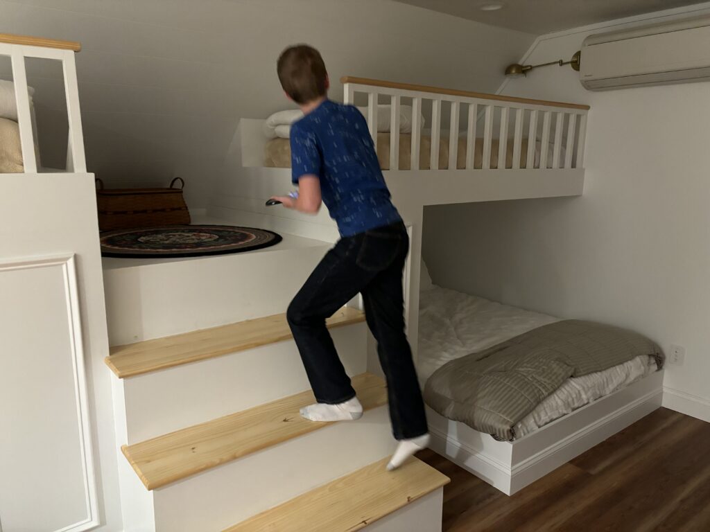 a boy walking up stairs in a room with a bunk bed
