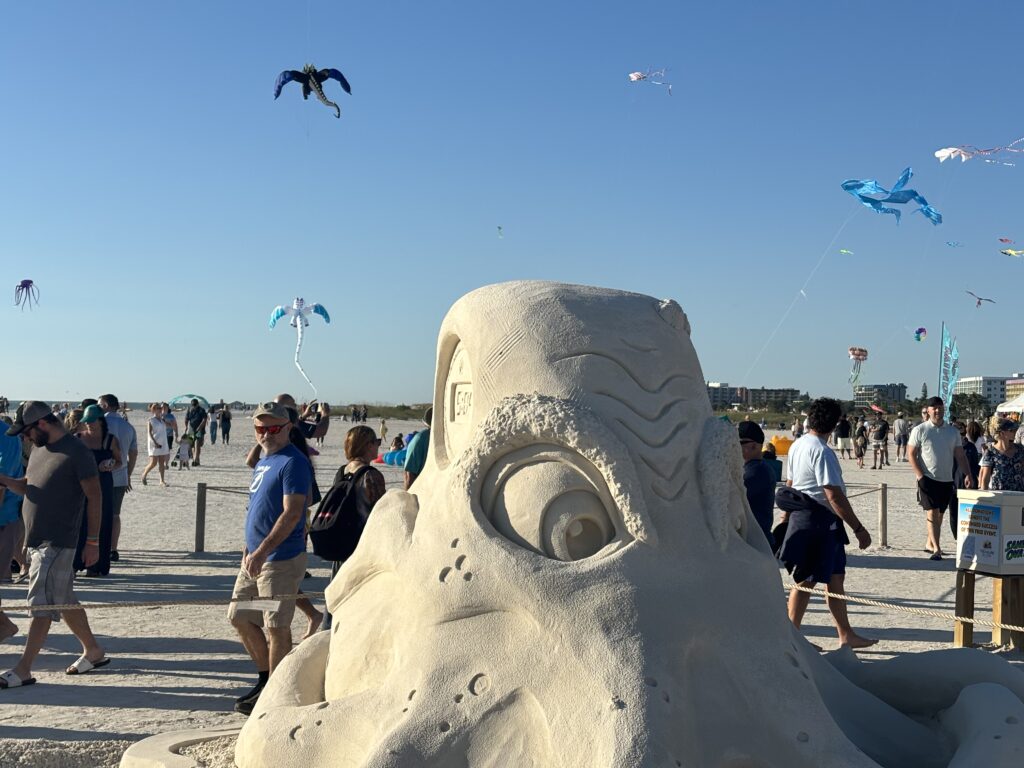 a sand sculpture of a monster with people flying kites