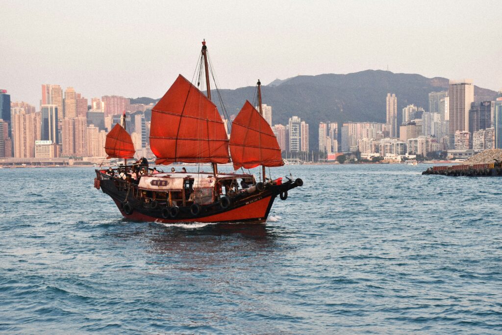 a boat with red sails on water with city in the background
