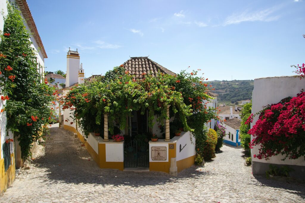 a small white and yellow building with a green roof and a red flower