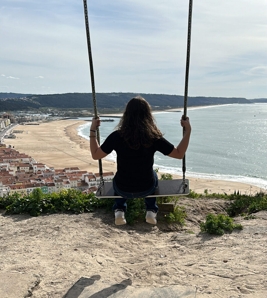 a woman sitting on a swing overlooking a beach