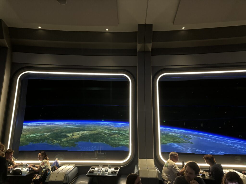 a group of people sitting at a table in a room with a large screen with a planet earth