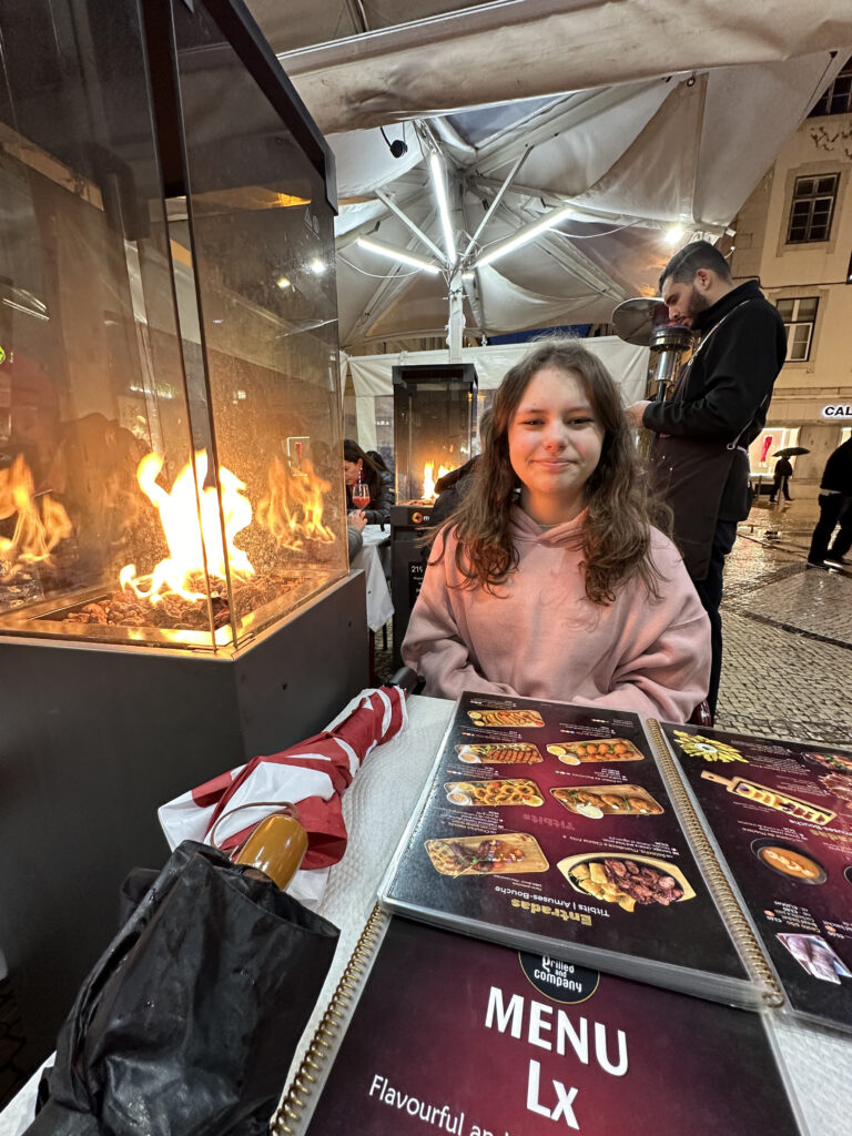 a girl sitting at a table with a fire in front of her
