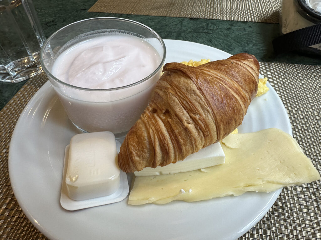 a plate of food with a glass of milk and a croissant