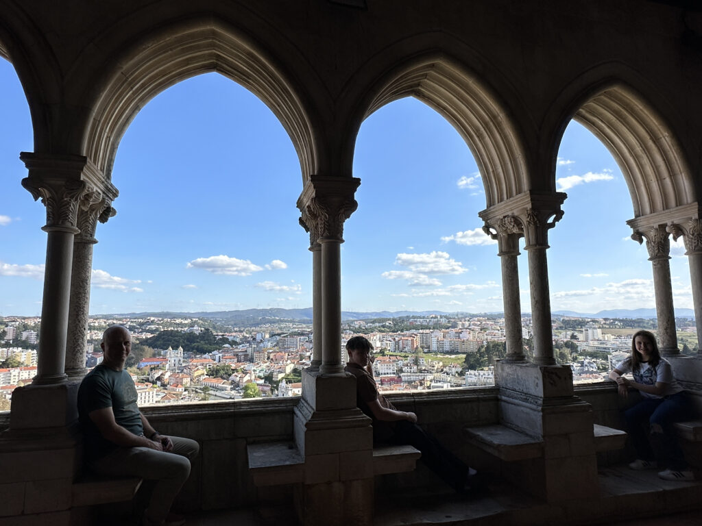 people sitting on benches in a building with arches and a city in the background