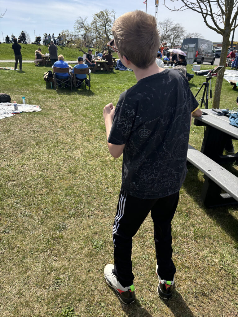 a boy standing in a grassy area with people sitting around