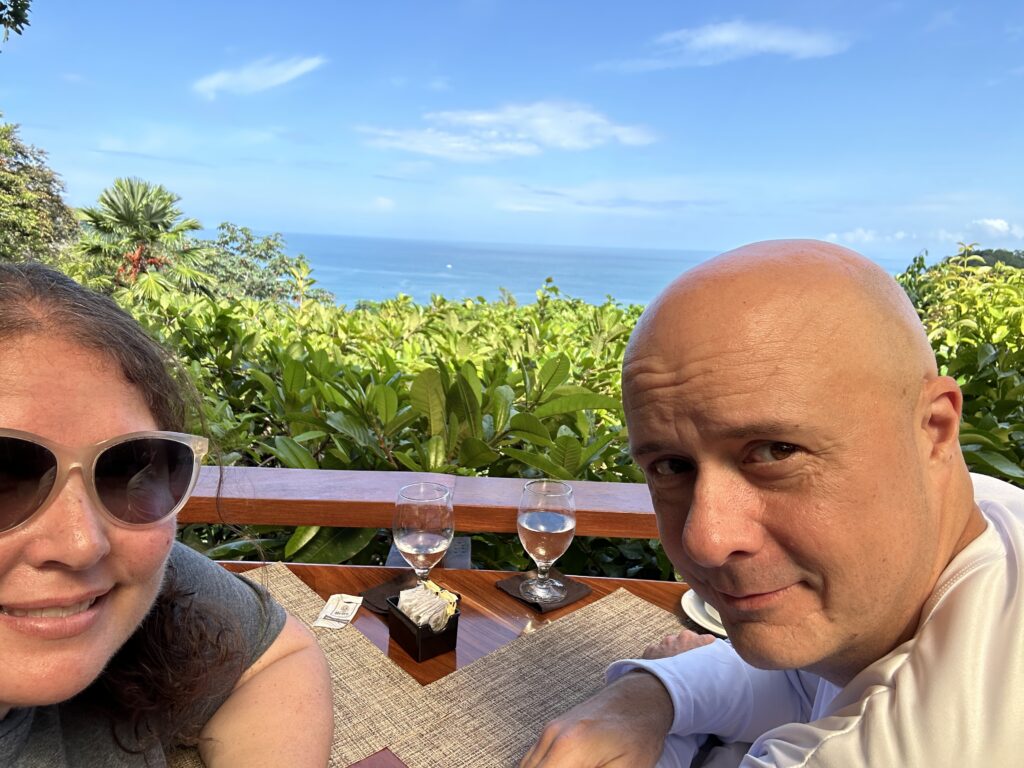 a man and woman sitting at a table with a view of the ocean