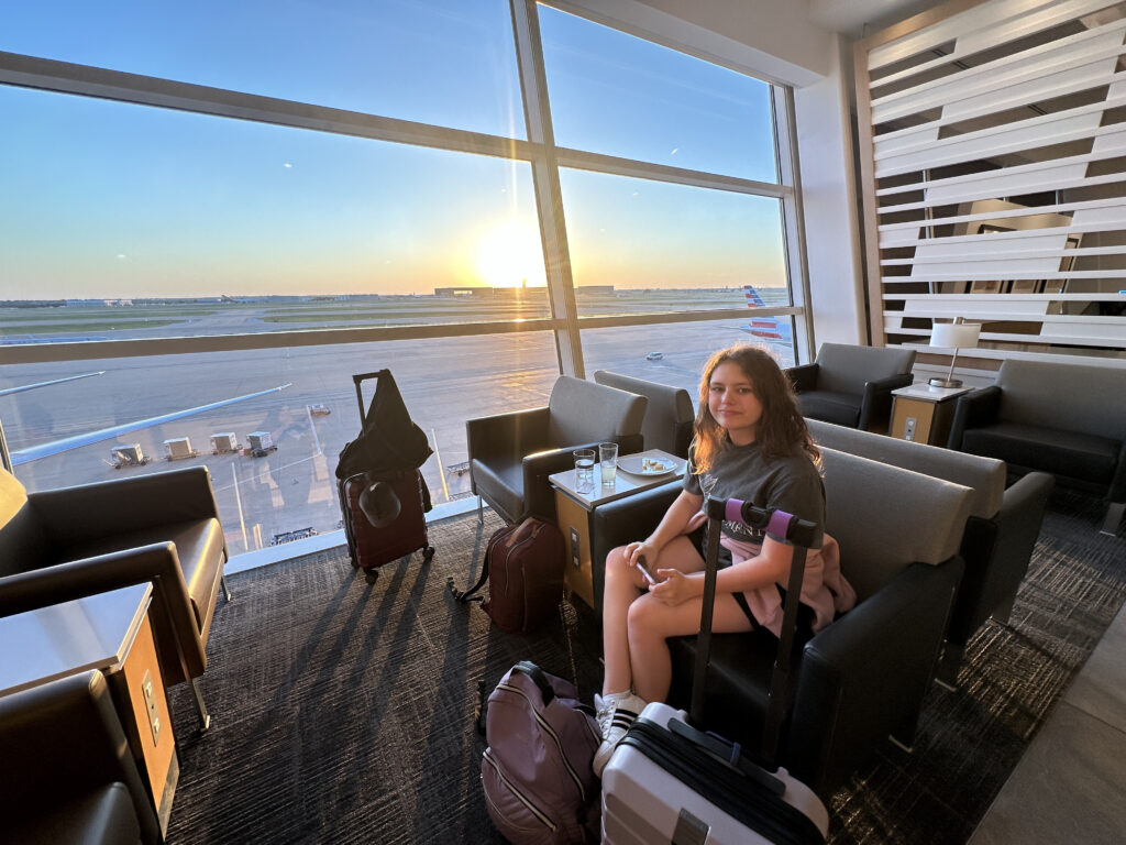 a girl sitting in a chair with luggage in front of a window