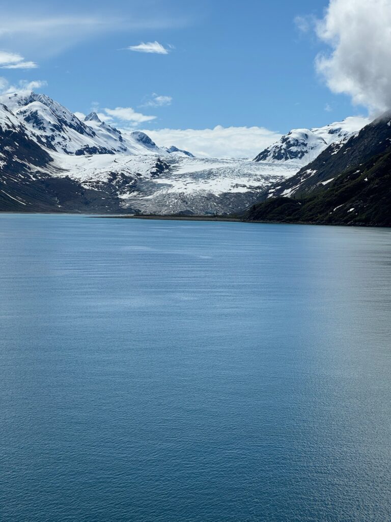 a body of water with snow covered mountains and clouds