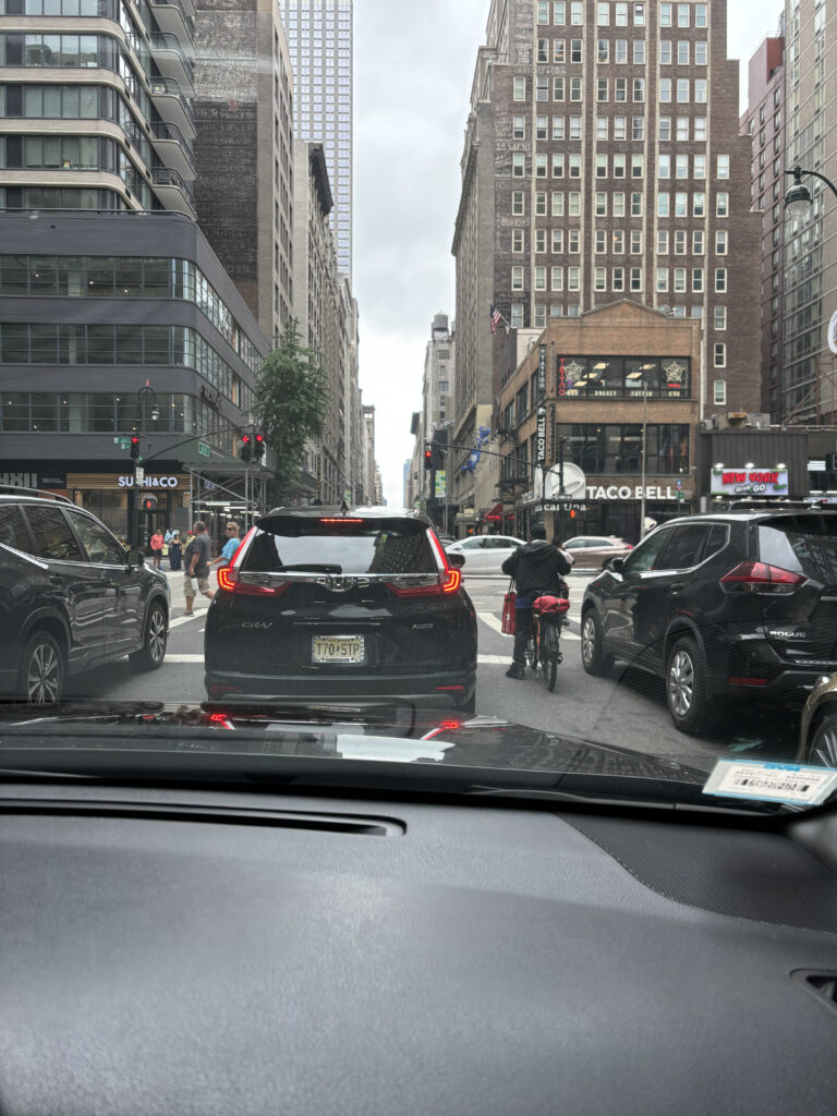 a view from a car window of a city street with cars and people