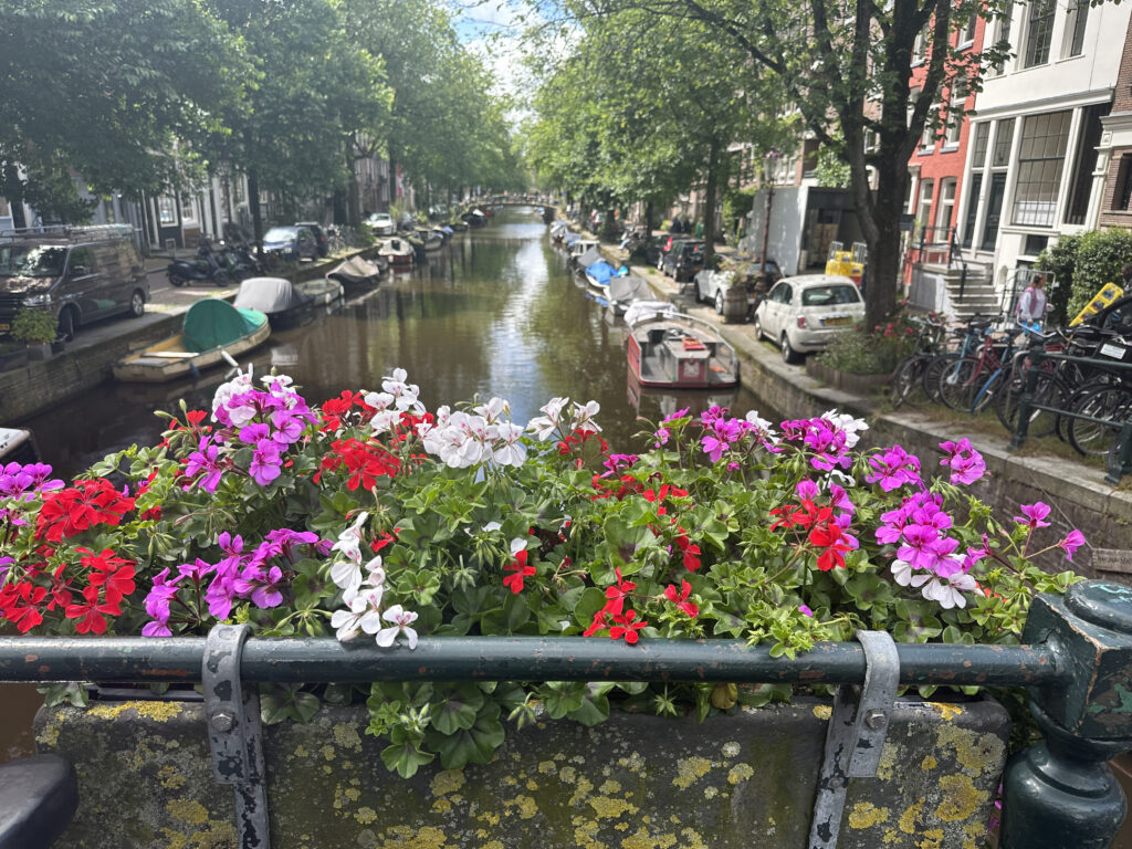 a flower pot with flowers on a railing over a canal with boats and buildings