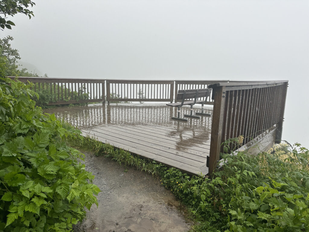 a wooden deck with a bench and a railing on a rainy day
