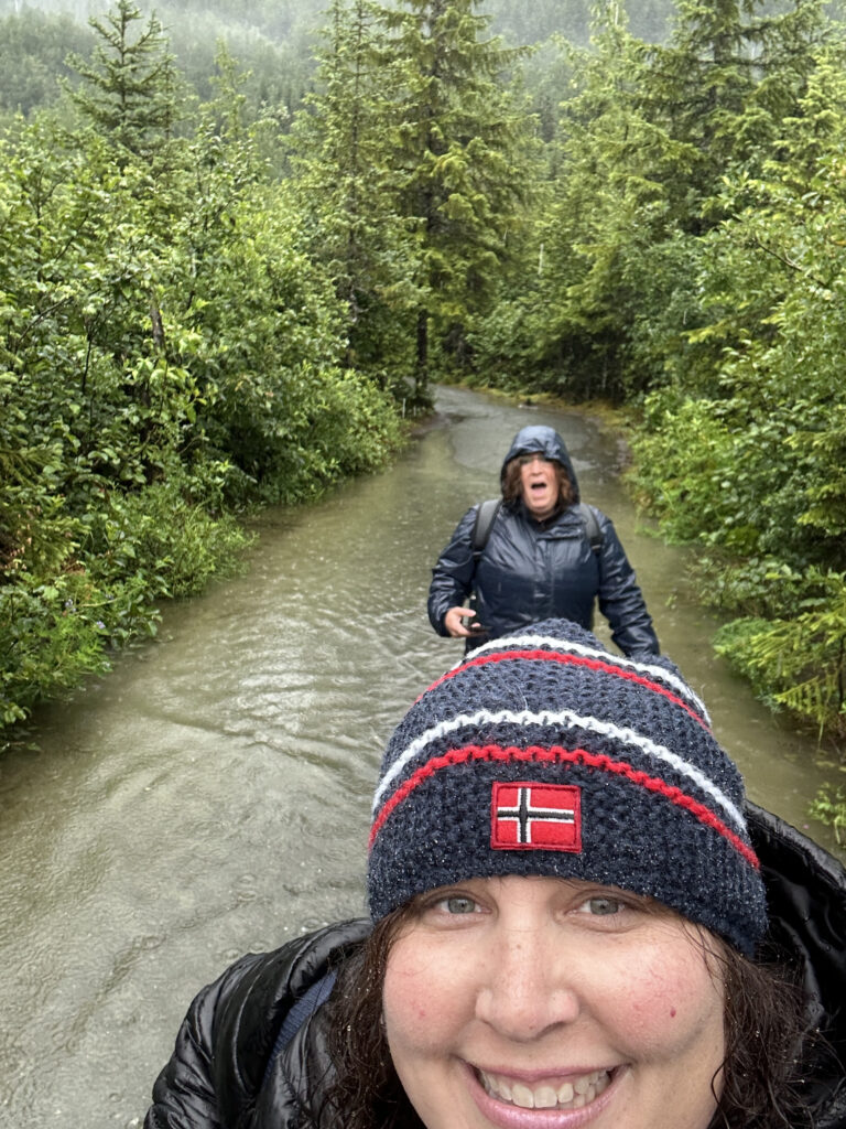 a woman taking a selfie in a river with a woman in a raincoat