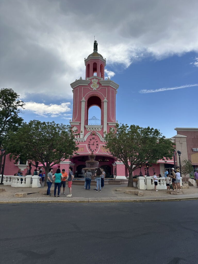 a pink building with a clock tower and people standing in front of it