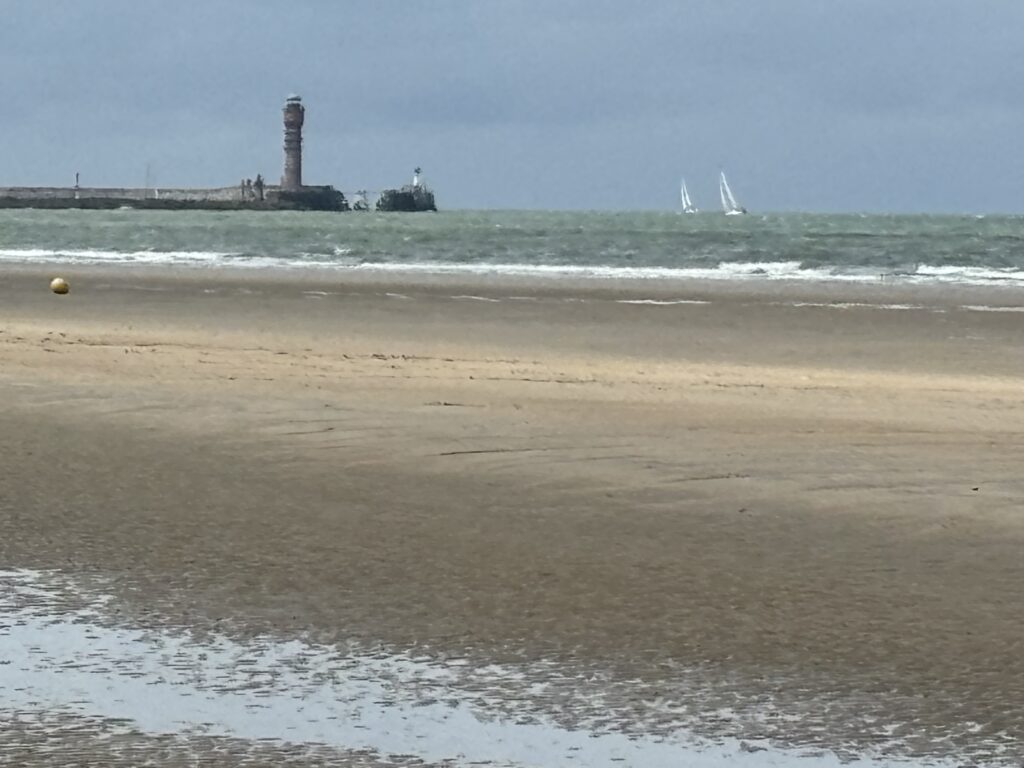 a beach with a lighthouse and sailboats