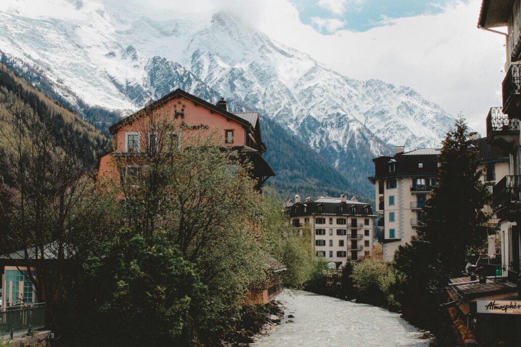 a river running through a town with trees and mountains in the background