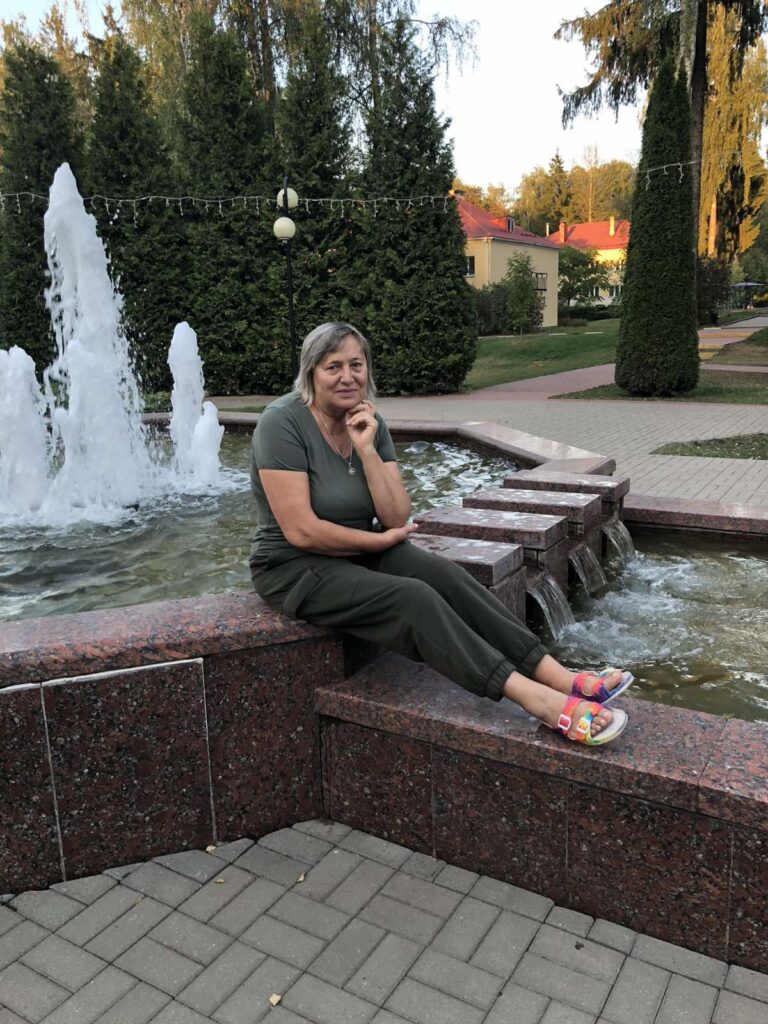 a woman sitting on a ledge with a fountain in the background