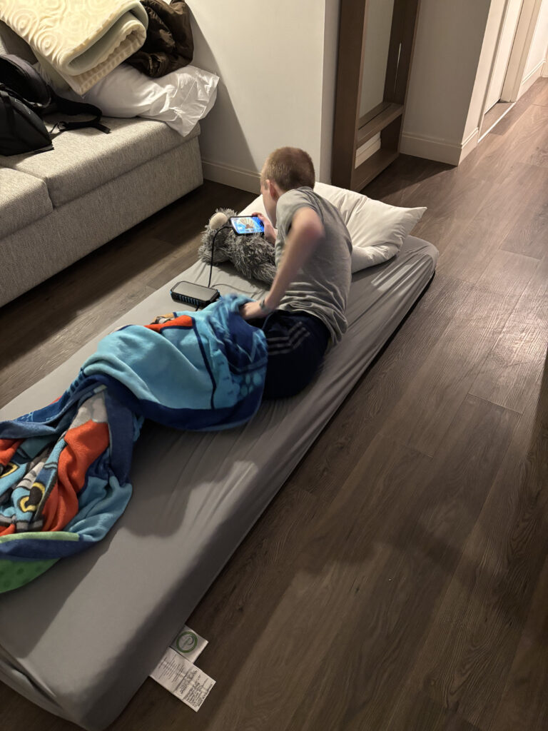 a boy lying on a bed with a blanket and a phone