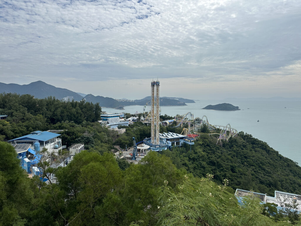 a large tower on a hill with trees and water in the background with Ocean Park Hong Kong in the background