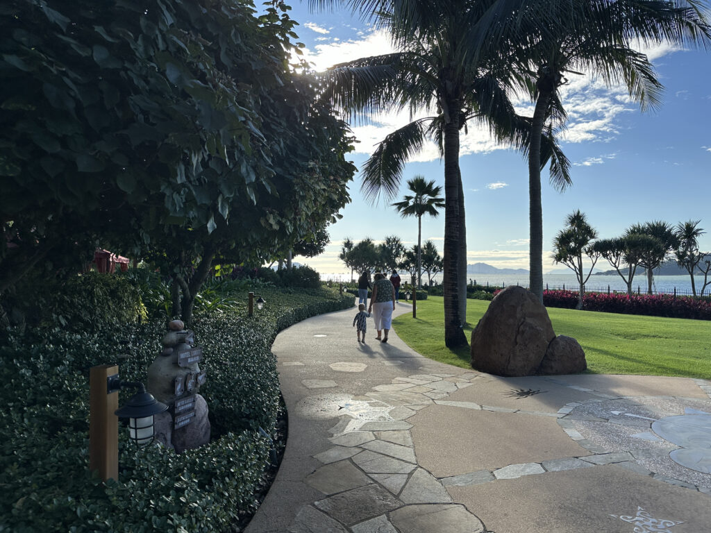 a group of people walking on a path with palm trees and a body of water