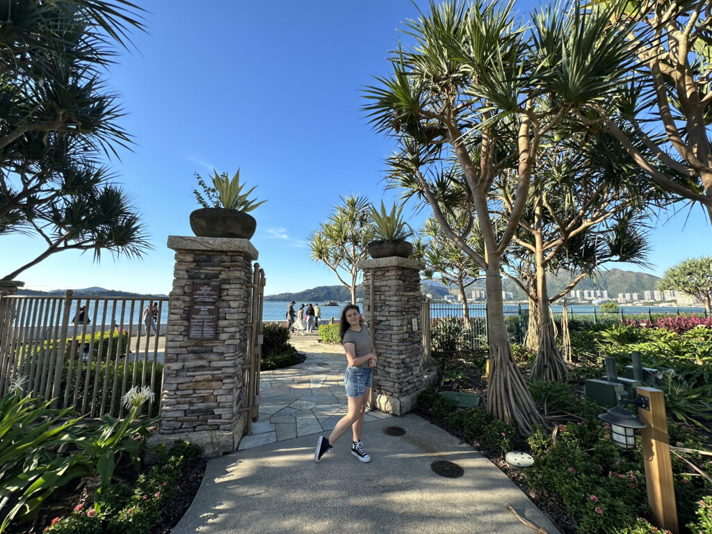 a woman standing in front of a stone gate with trees and a body of water