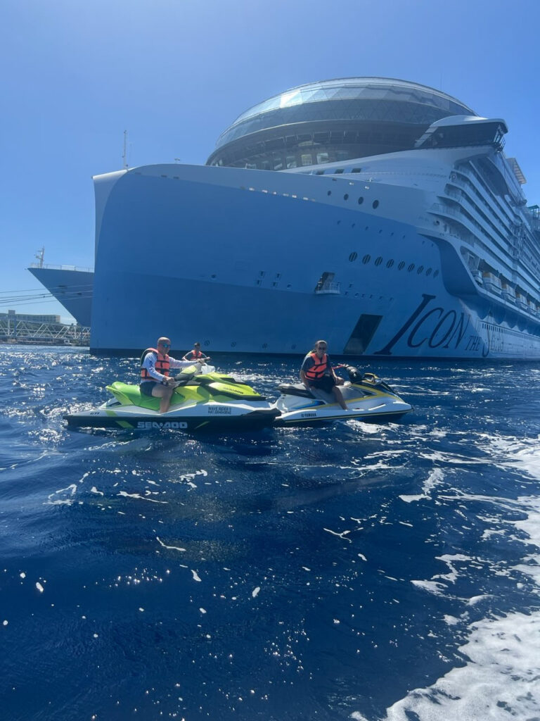 two people on jetski in the water with a large cruise ship in the background