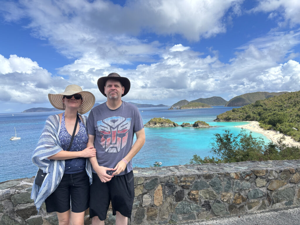 a man and woman standing on a stone wall with a beach and islands in the background