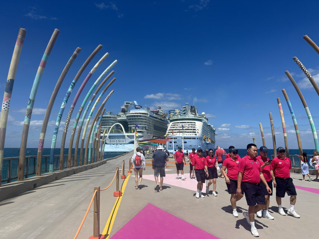 a group of people walking on a dock with a cruise ship in the background